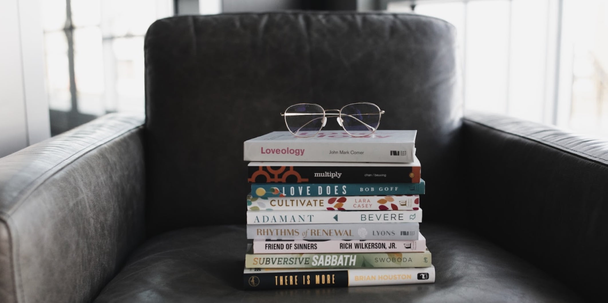 A stack of books on a chair with a pair of glasses folded on top of them